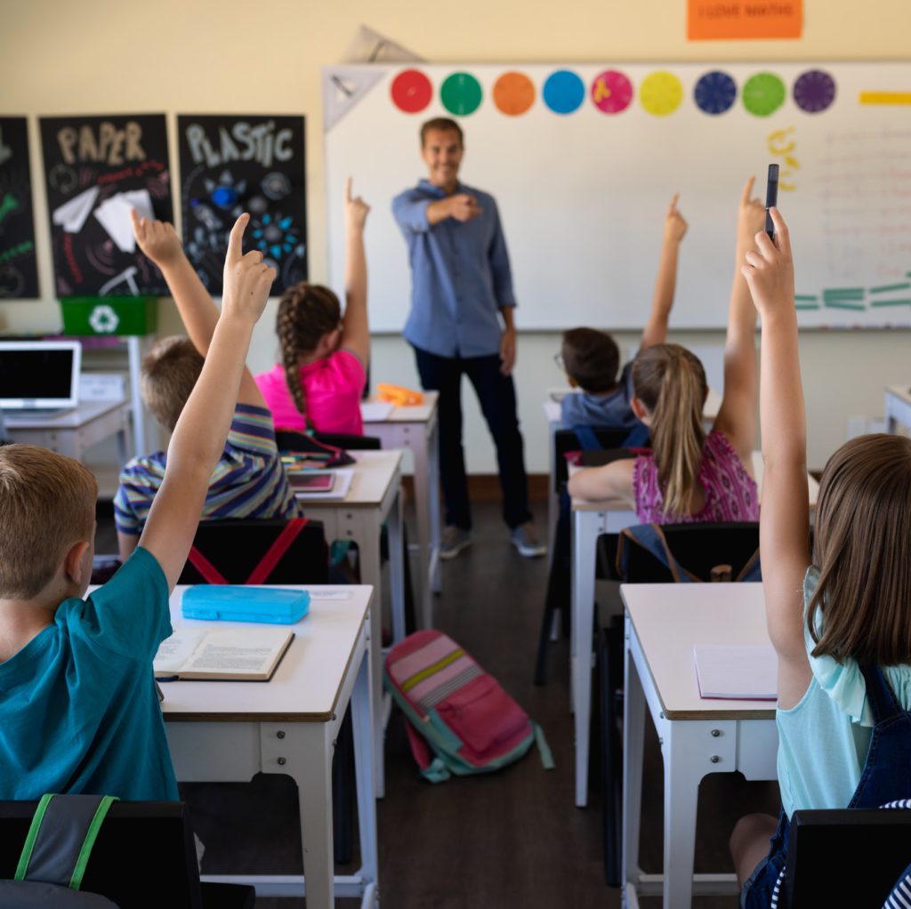 Male school teacher standing in an elementary school classroom with a group of school children