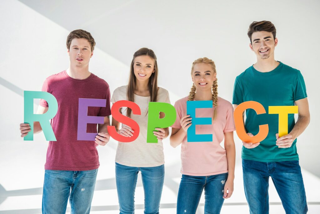 happy young friends holding colorful word respect and smiling at camera on grey